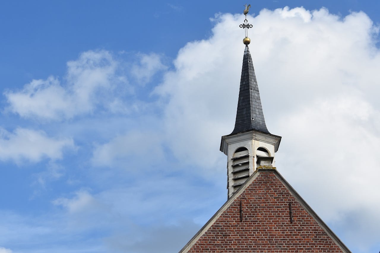 A classic chapel with a steeple, cross, and vibrant blue sky with clouds.
