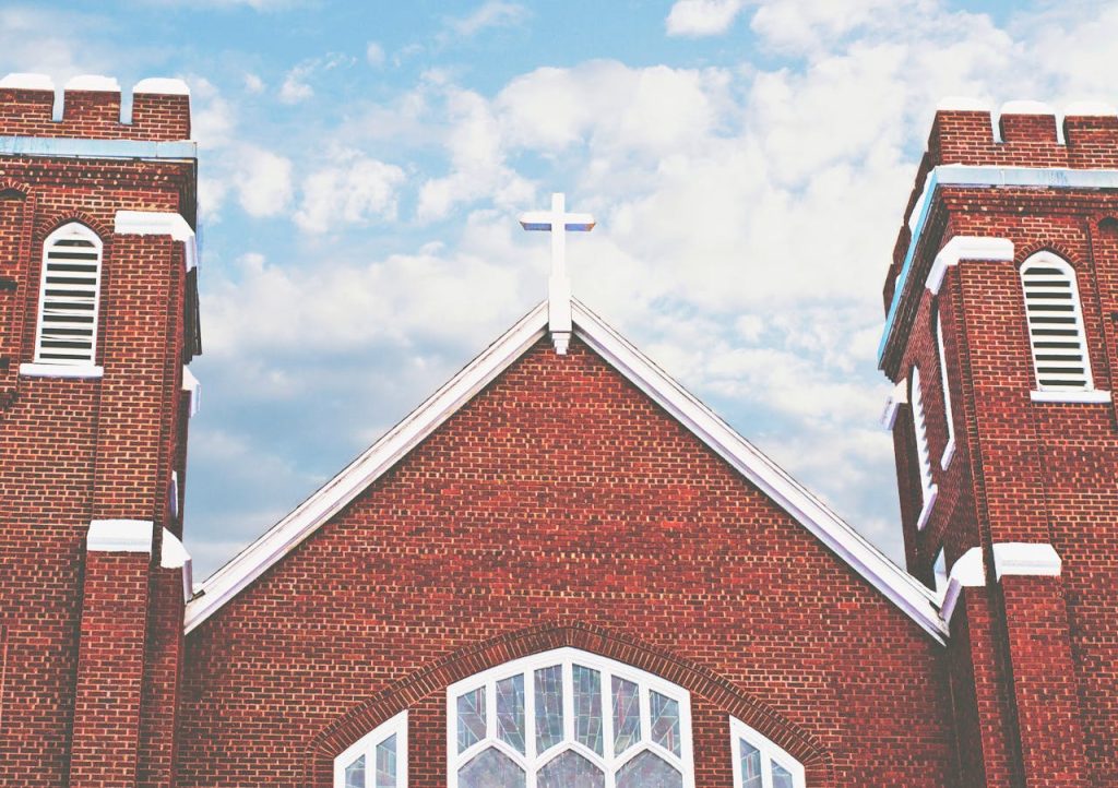 pexels photo 287332 Red brick church with a cross and arched windows under a blue sky with clouds.