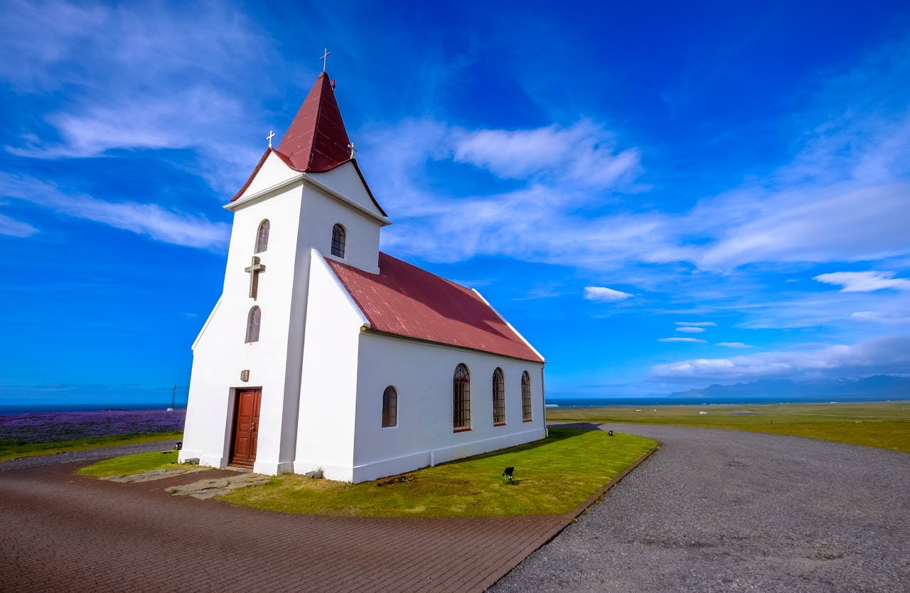 Beautiful white church set against a vibrant rural landscape with blue skies and lush grasslands.
